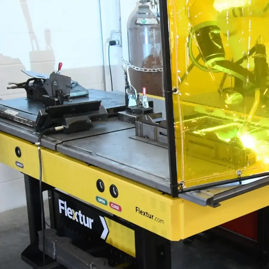 Flextur Cobot 36" x 36" Quick Change Table with Yellow Safety Shield and Cobot Welding Arm in Action.